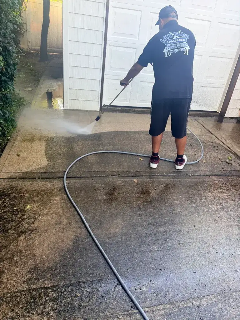 LIWC Pro technician pressure washing a concrete driveway beside a garage.