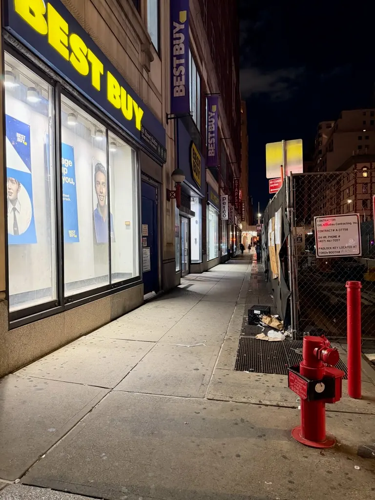 Retail storefront and sidewalk beside a red fire hydrant at night.